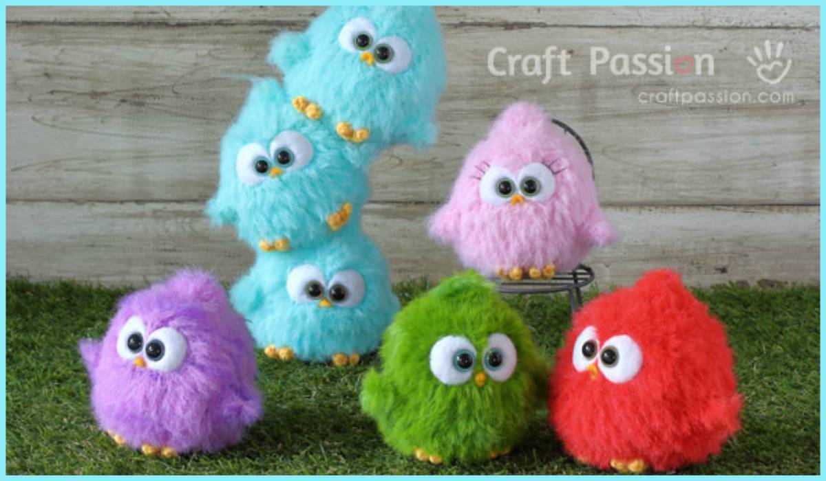 Five fluffy bird-shaped plush toys, reminiscent of a Fur Bird Amigurumi, in vibrant colors like blue, pink, purple, green, and red rest charmingly on grass. The three blue ones are stacked in a playful manner.