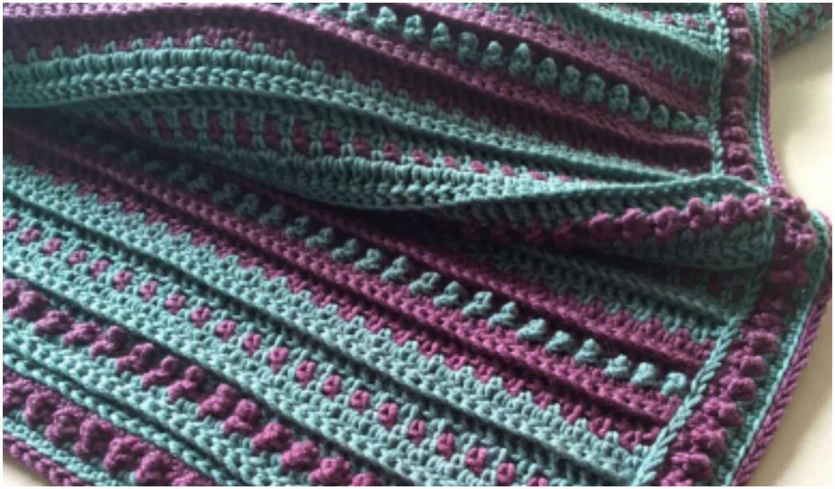 Introducing the Northling Blanket: a crochet masterpiece with alternating stripes of purple and teal yarn, featuring a textured pattern. This project comes with a free crochet pattern to guide you through every step.