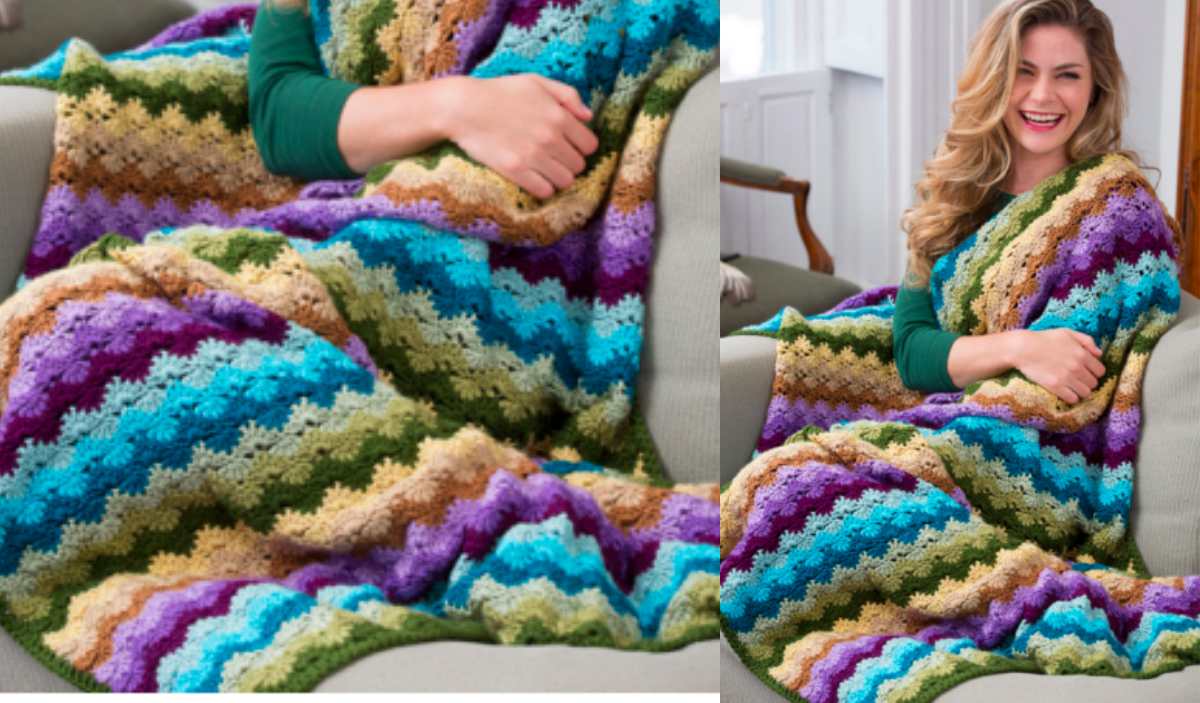 A person in a green shirt is wrapped in a vibrant Twilight Shells Throw, showcasing its intricate crochet pattern with zigzag designs, while sitting comfortably on a couch.