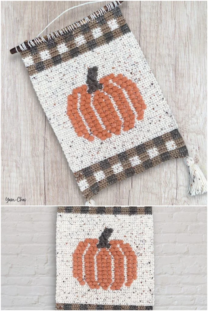 Crocheted wall hanging with an orange pumpkin pattern, brown and cream plaid borders, and a wooden rod with tasselsโperfect as one of your crochet decorations for fall.