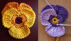 Two crocheted flowers: one yellow and orange, the other reminiscent of pansy flowers in purple and lavender. A crochet hook is inserted into the purple flower, hinting at free crochet patterns ready to inspire your next creative project.