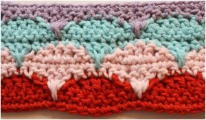 Colorful crochet pattern with rows of scallop designs in red, pink, light blue, and purple yarn, reminiscent of a clamshell afghan.