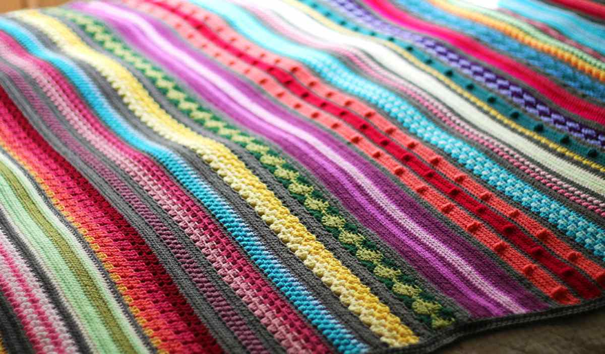 Introducing the Rainbow Sampler Blanket, a colorful crocheted masterpiece with horizontal stripes in vibrant patterns. This delightful creation features shades of red, blue, green, yellow, and purple. Dive into the crochet pattern and create your own free pattern-inspired treasure.