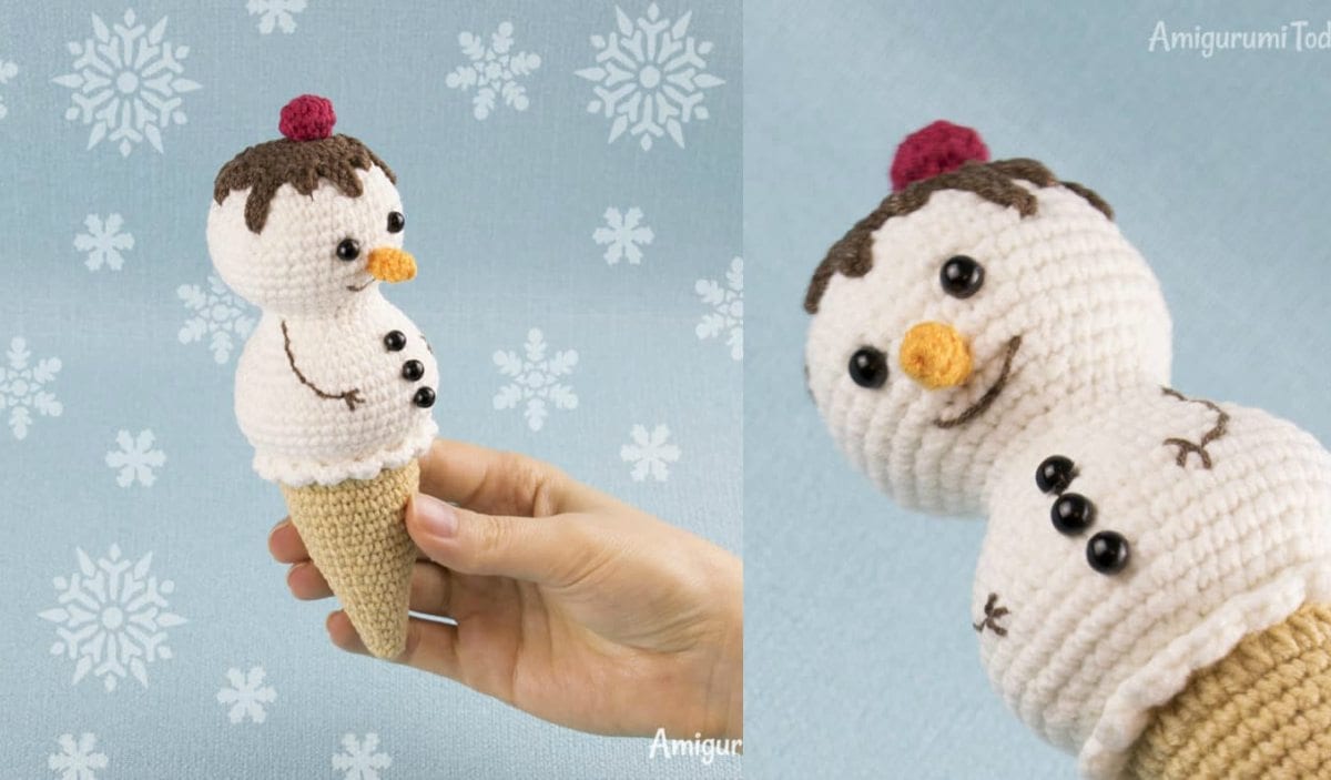 A hand holding a crochet Ice Cream Snowman, complete with a carrot-shaped nose and black buttons. The snowman sits atop an ice cream cone base adorned with chocolate topping. The background is light blue with white snowflake patterns, adding a touch of winter magic.