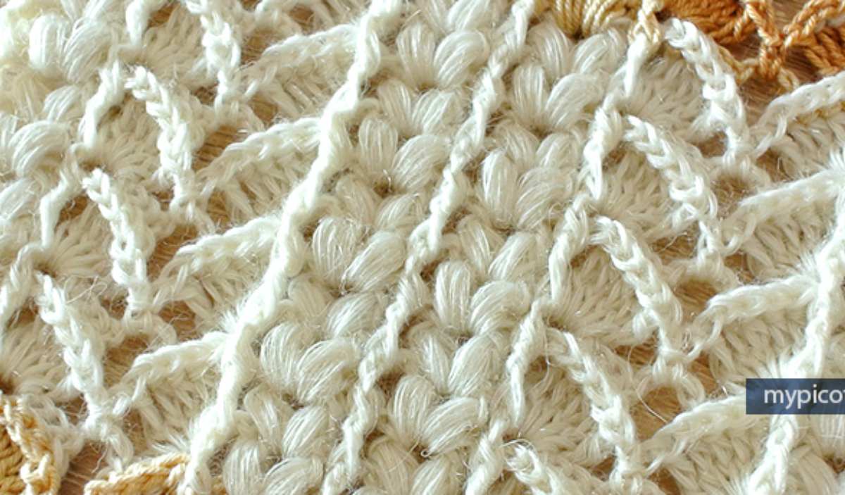 Close-up of a textured, white knitted fabric with a diamond pattern, showcasing intricate detailed stitches reminiscent of a textured puff stitch, perfect for those seeking inspiration for their next free crochet pattern.