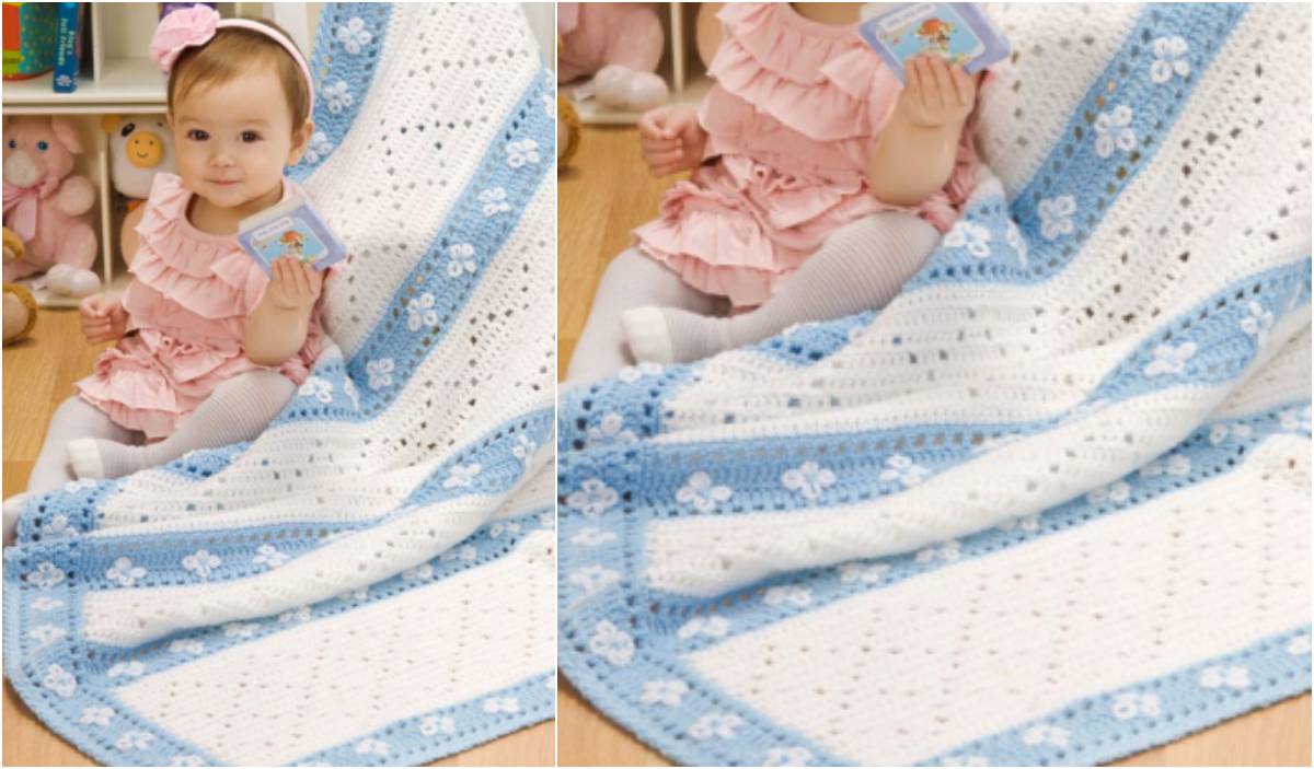 A baby in a pink dress sits on a blue and white baby blanket featuring a lazy daisy crochet pattern, holding a small book, with stuffed toys in the background.