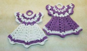 Two vintage dress potholders, crocheted in purple and white, grace a light surface with charm.