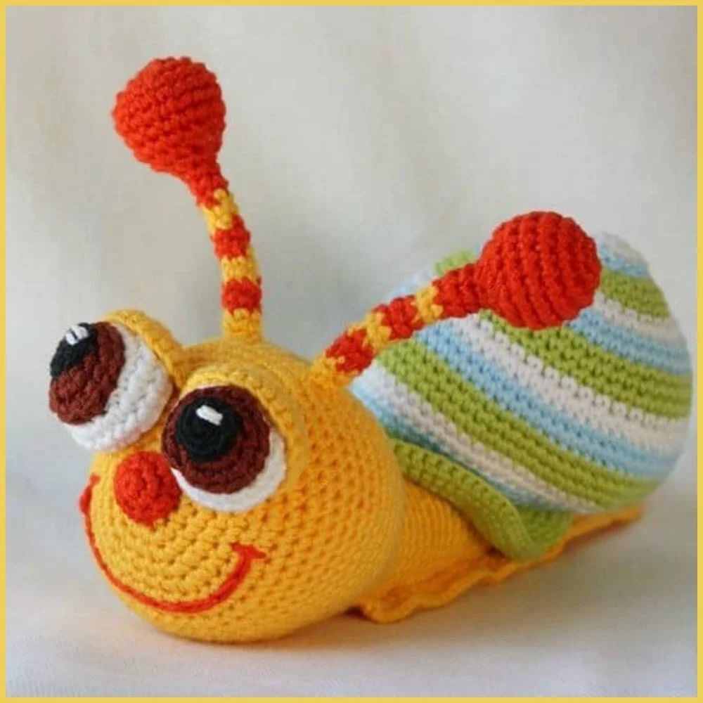 This amigurumi crocheted caterpillar toy features large eyes, red antennae, and a striped body in yellow, blue, and green.