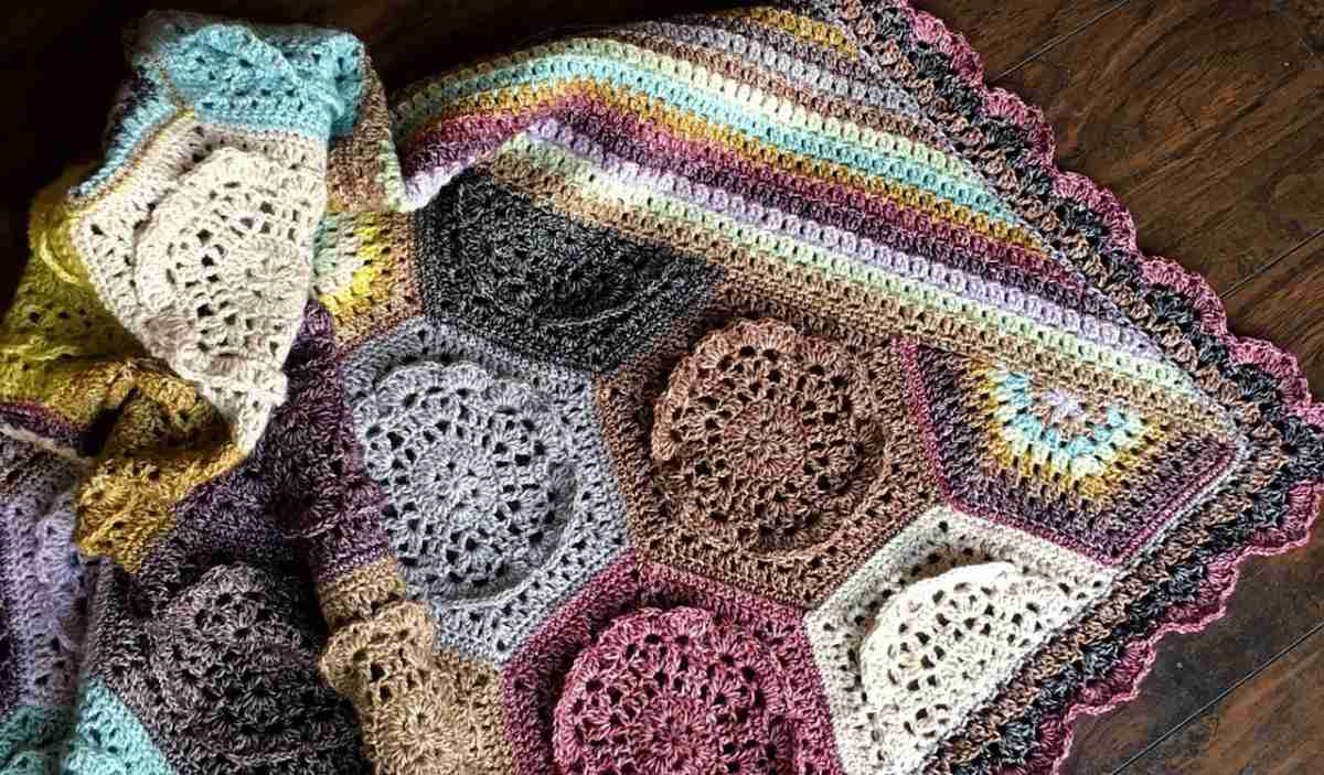 A colorful crocheted blanket featuring hexagonal and round patterns in various yarn colors, reminiscent of a Dutch Rose Throw, is elegantly draped over a wooden surface.