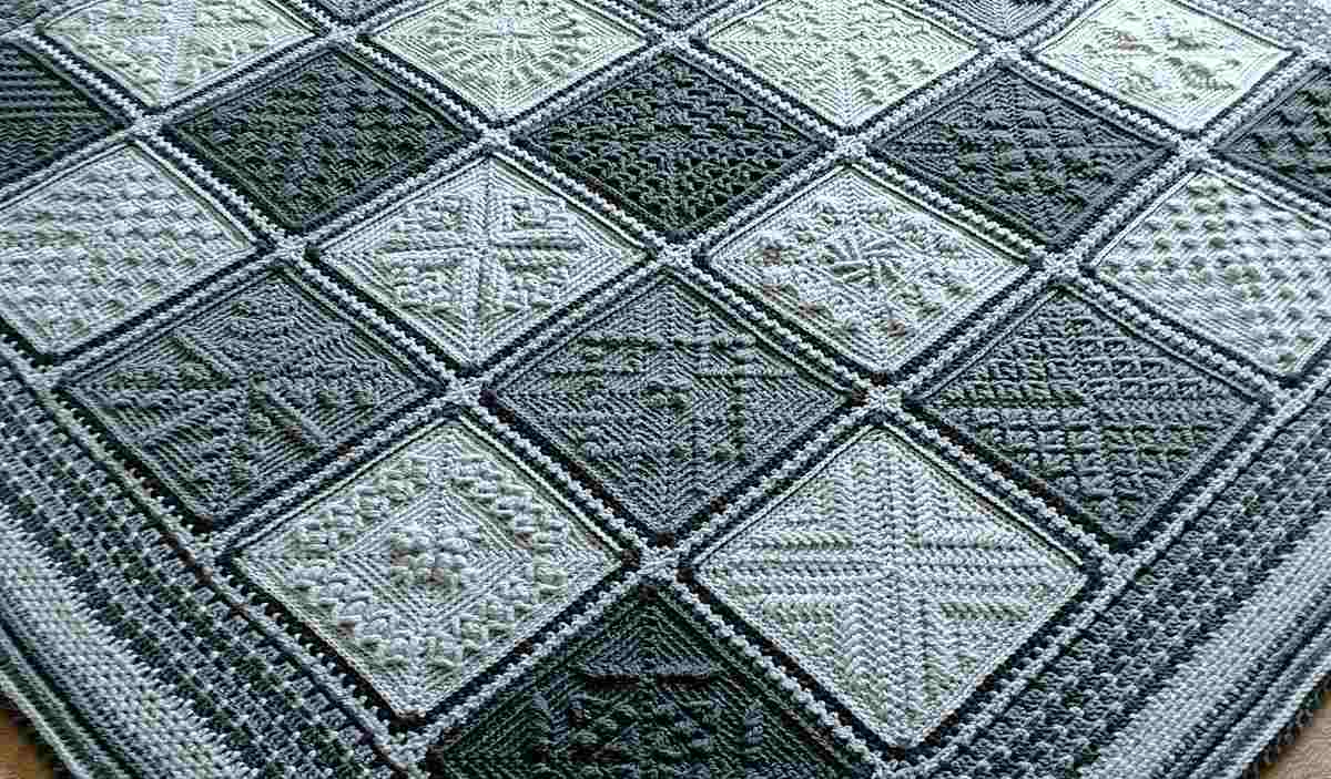 A textured gray and green knitted blanket, reminiscent of stardust melodies, features a crochet pattern with diamond-shaped squares, each adorned with unique intricate designs.