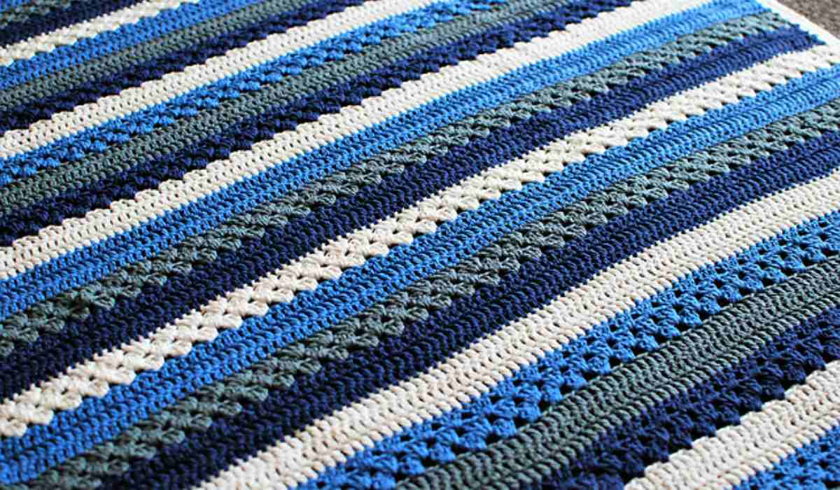 The Tasmanian Baby Blanket features crocheted horizontal stripes in shades of blue, green, and white. Perfect for any nursery, this design comes with a free pattern for easy crafting.