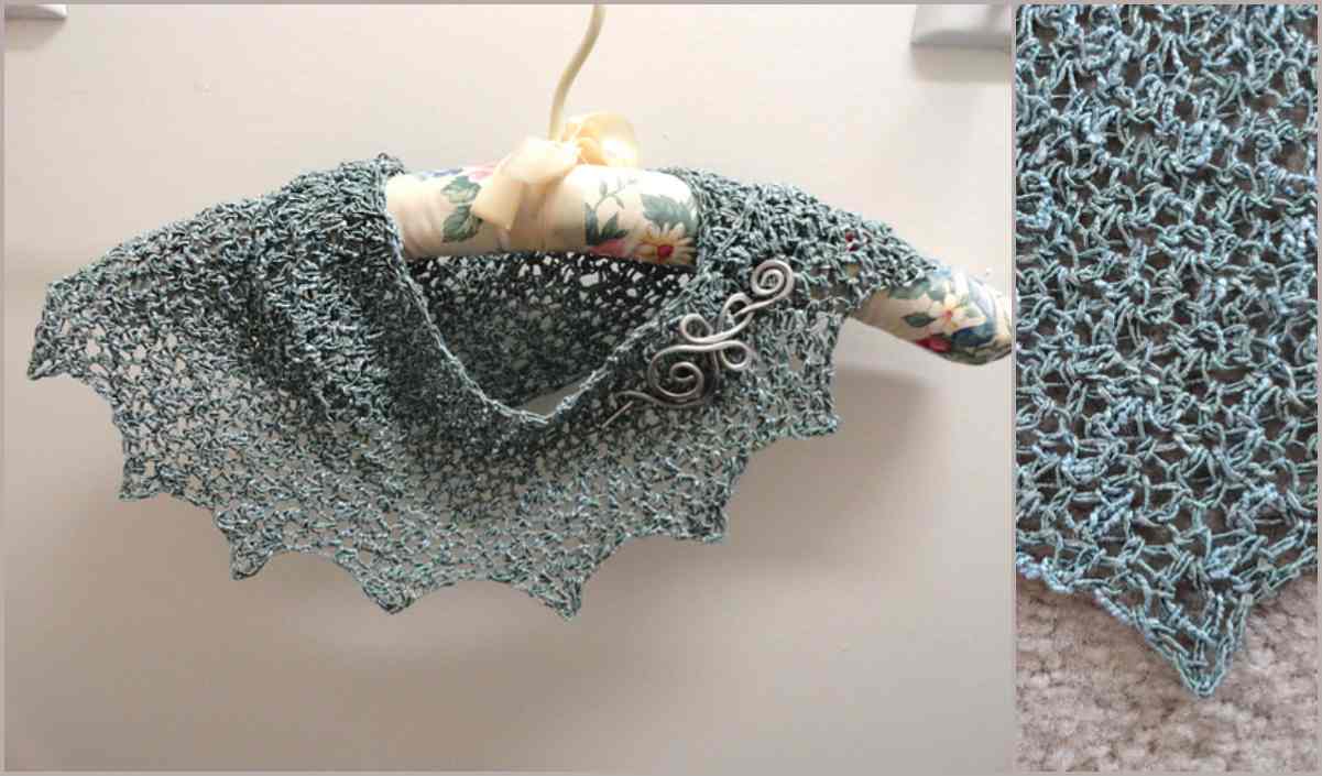 A light blue, intricately knitted Snow Drop Shawl hangs on a floral padded hanger, showcasing a detailed pattern and edged trim.