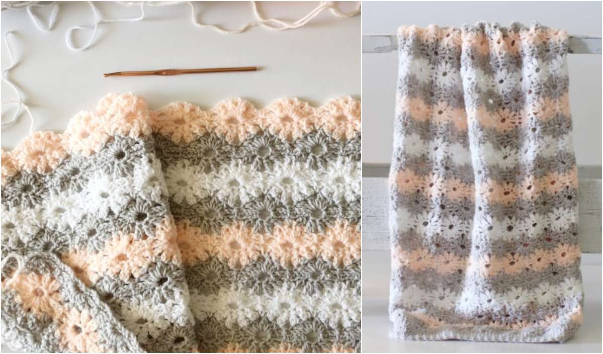 Crocheted baby blanket showcasing a delicate petal stitch with alternating stripes in gray, white, and peach hues, featuring a scalloped edge. A crochet hook lies nearby.