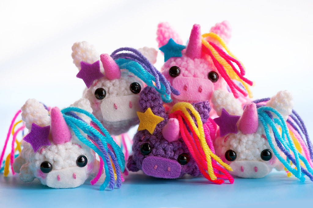 A group of five crocheted unicorn toys, made using free unicorns crochet patterns, with colorful yarn manes, large black eyes, and star decorations, arranged against a blue background.