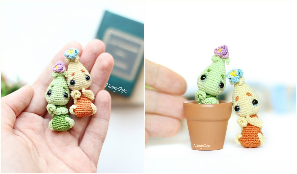 Two miniature crochet creatures, one green and one orange, with small flowers on their heads, evoke a sense of whimsy. These charming Kawaii onions are displayed on a hand next to a small plant pot, perfect for those seeking creative inspiration or a unique crochet pattern.