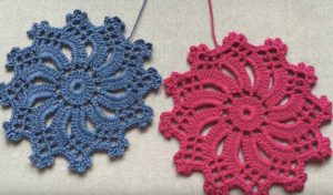 Two crocheted doilies, one blue and one pink, with intricate floral patterns reminiscent of dragon scales, placed on a light surface.