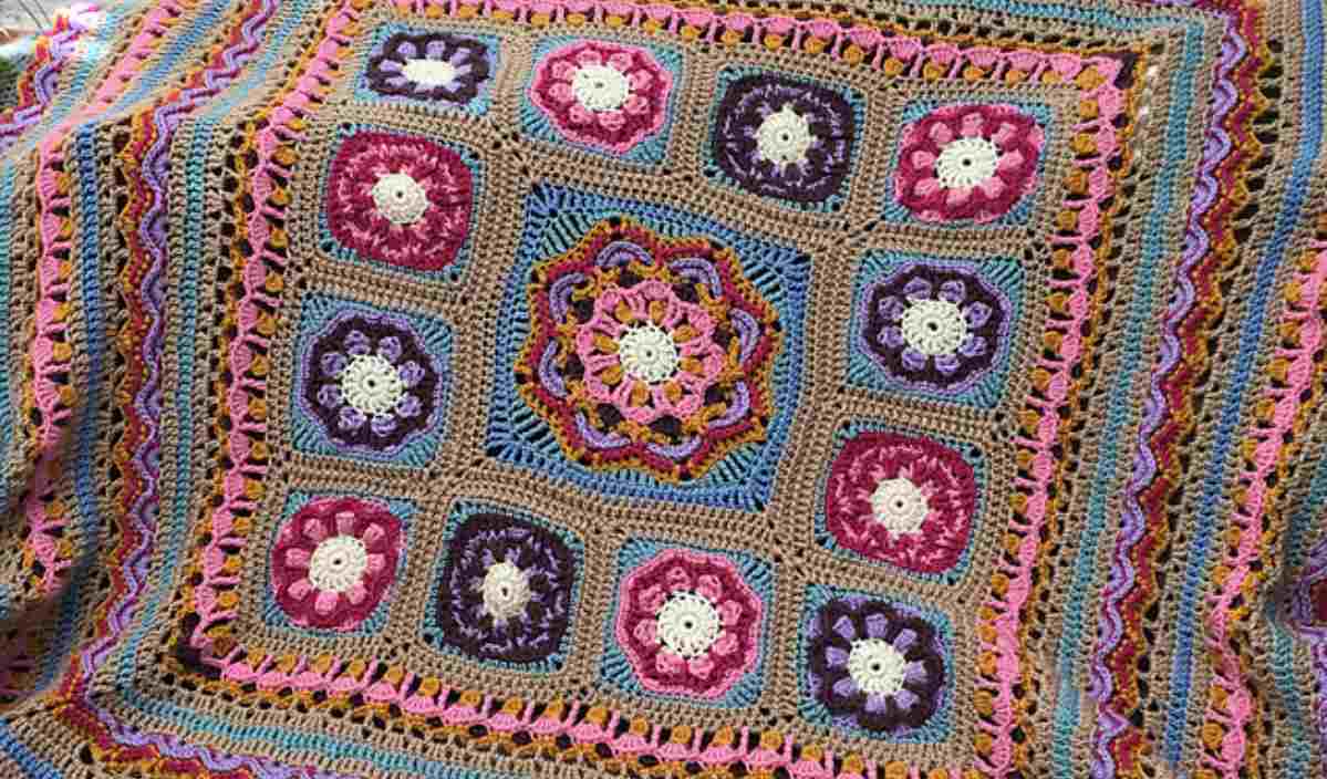 The Beaulieu Blanket is a colorful, crocheted blanket featuring square floral patterns and decorative borders in various colors. Explore the free crochet pattern to bring this vibrant masterpiece to life.