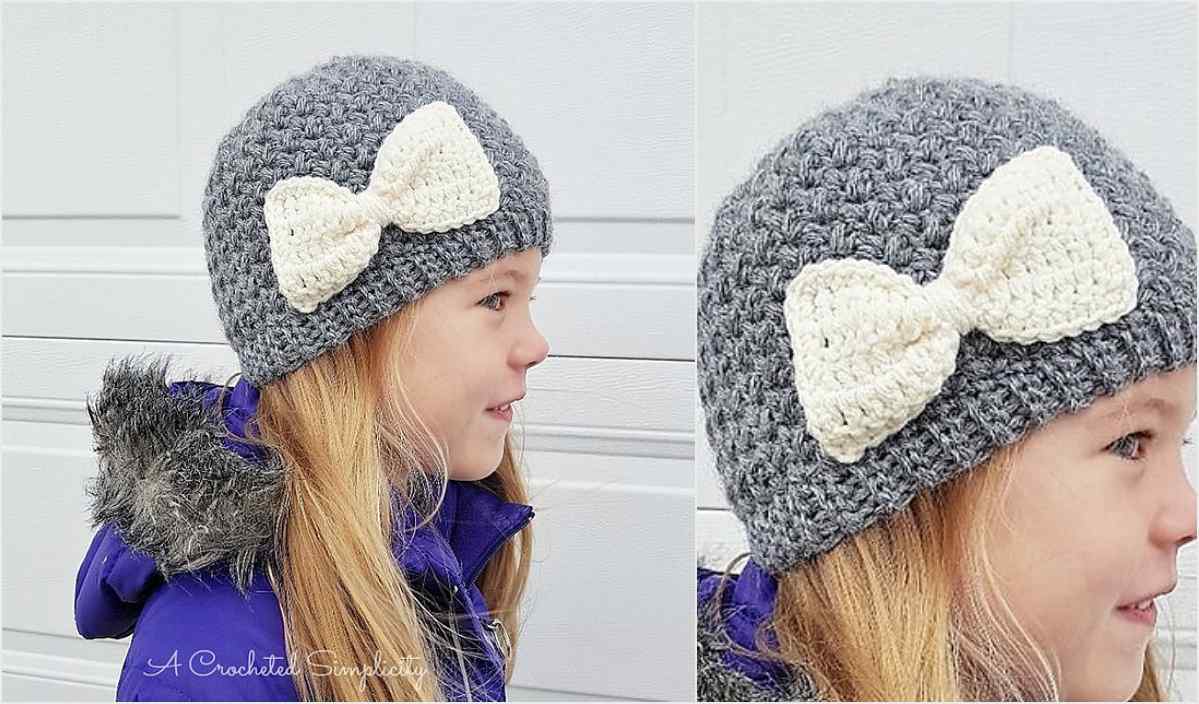 A child wearing a gray crocheted beanie with a large white bow stands against a light-colored wall, reminiscent of the delightful patterns found in crochet donut designs.