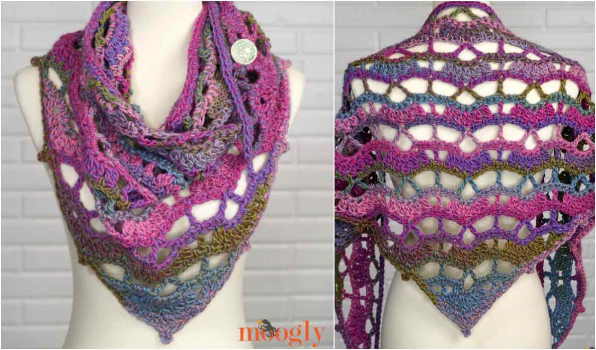 A mannequin showcases a vibrant crocheted triangular shawl, adorned with a lace pattern in shades of pink, purple, and green. This exquisite piece is beautifully captured from front and back against a white brick background—a perfect find for those seeking crochet pattern inspiration.