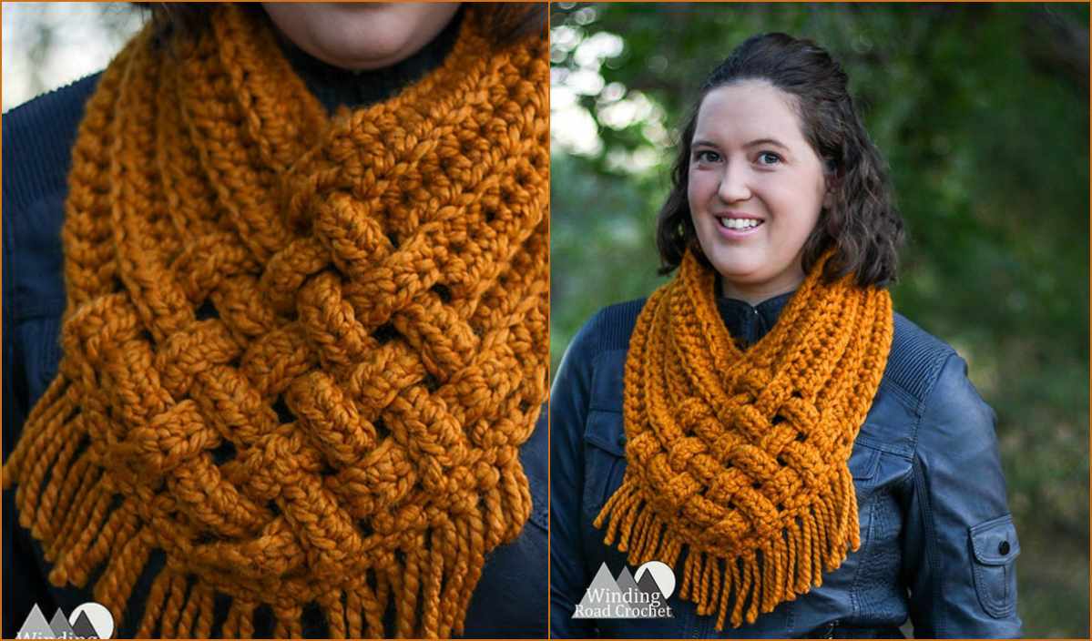 A person is standing outdoors, wrapped in a thick, mustard-yellow crocheted scarf featuring an intricate crochet pattern with fringe.