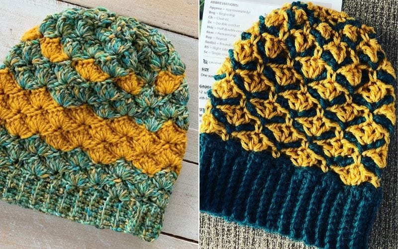 Two crocheted Shell Stitch Beanies with intricate patterns rest on a wooden surface; one showcases vibrant blue and ochre, while the other features soothing teal and yellow.