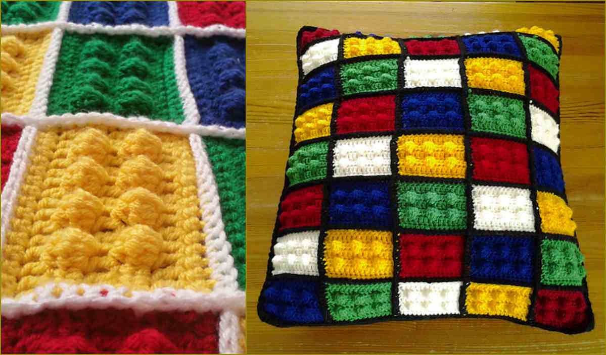 A vibrant, crocheted Lego Block Pillow featuring a patchwork design of red, yellow, green, white, and blue squares. The close-up reveals intricate cable stitching on a yellow square.