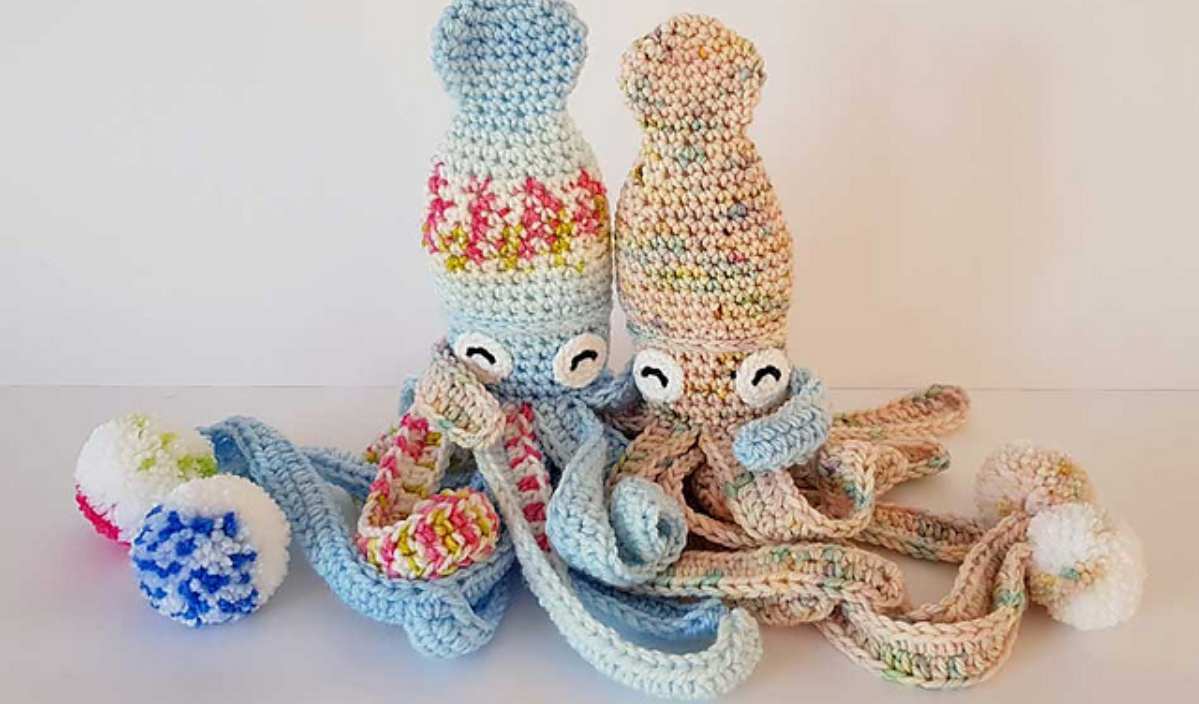 Two crocheted squid toys, affectionately named Hubble the Squid, flaunt their colorful tentacles and stylish beanies while sitting on a white surface. Their charm is undeniable, making you wonder if there's a free crochet pattern available to create your own vibrant companions.