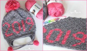A gray knitted hat with "2019" in pink yarn and a pom-pom, displayed alongside colorful yarn balls and a crochet hook, perfect for C2C Crochet enthusiasts seeking inspiration from a free pattern.