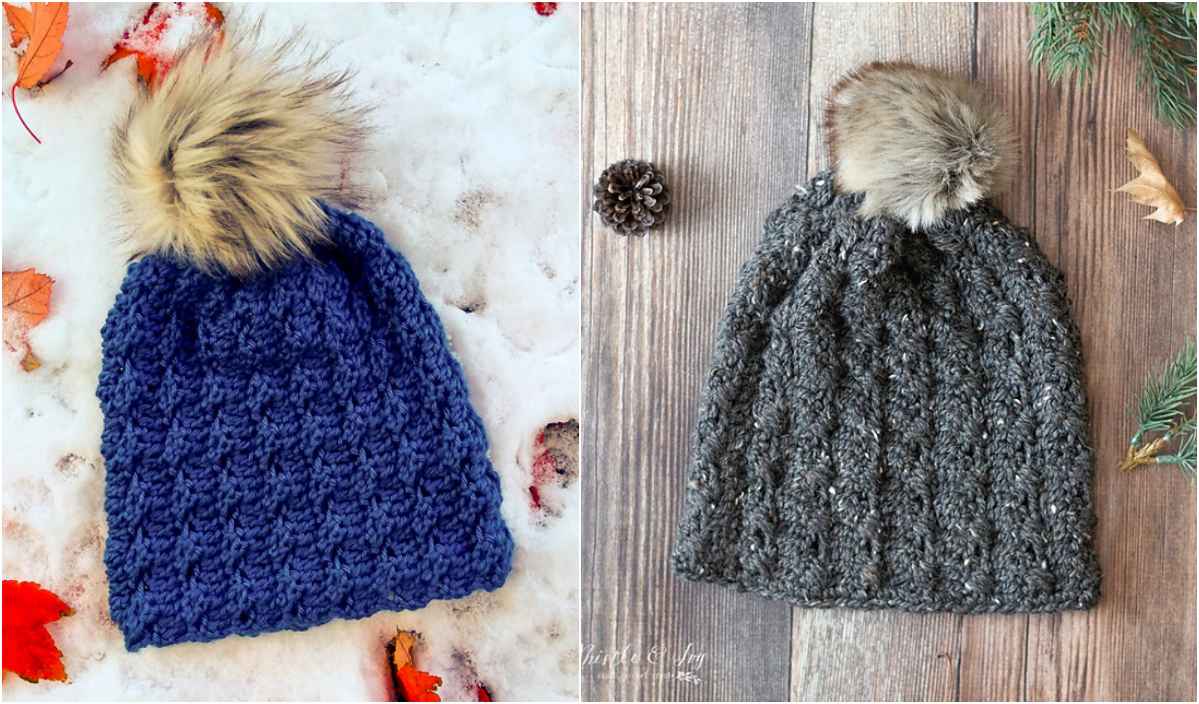 Two knitted beanies with faux fur pom-poms: a blue one on snow and a gray Cobblestone Hat on a wooden surface adorned with pine cones and leaves.