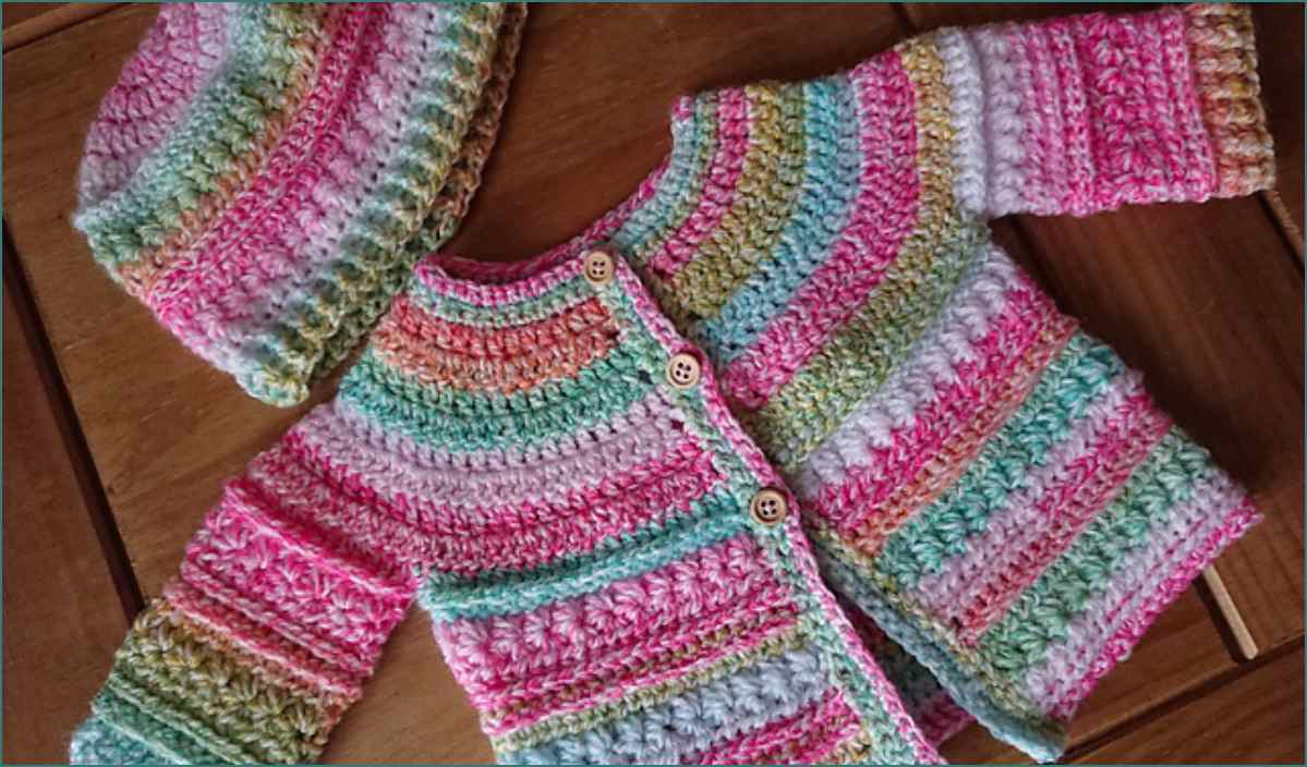 A delightful crocheted baby sweater and hat set featuring multicolored pastel stripes rests on a wooden surface, crafted from a charming Csenge Anna crochet pattern.