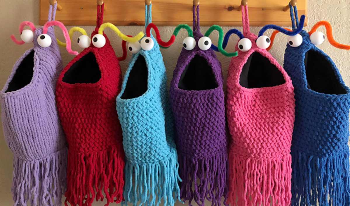 Colorful knit bags with googly eyes and fringes hang on hooks, featuring open mouth designs, pipe cleaner accents, and a playful nod to an Afghan Block style. Plus, discover a free crochet pattern to make your own quirky accessory.