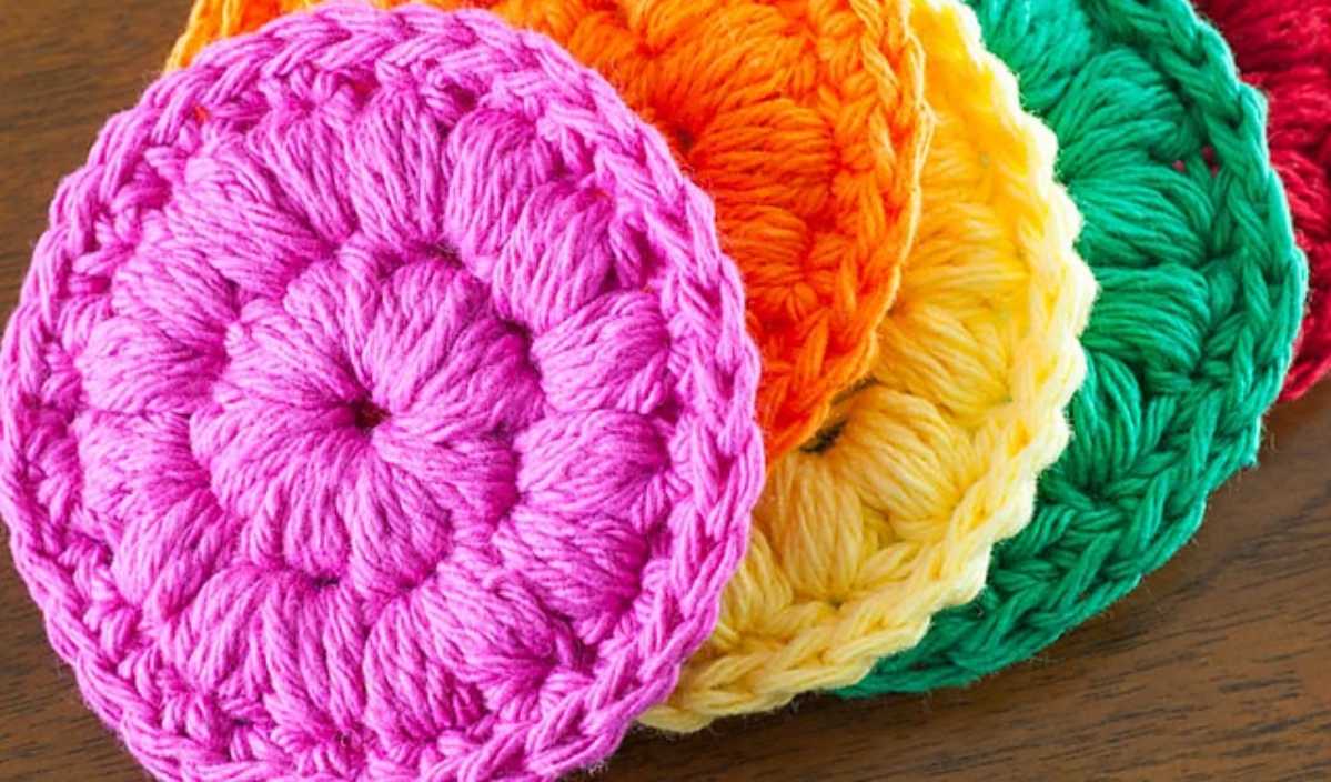 Colorful crocheted coasters, crafted with a delightful crochet pattern, are arranged in overlapping layers, showcasing pink, orange, yellow, green, and red hues on a wooden surface.