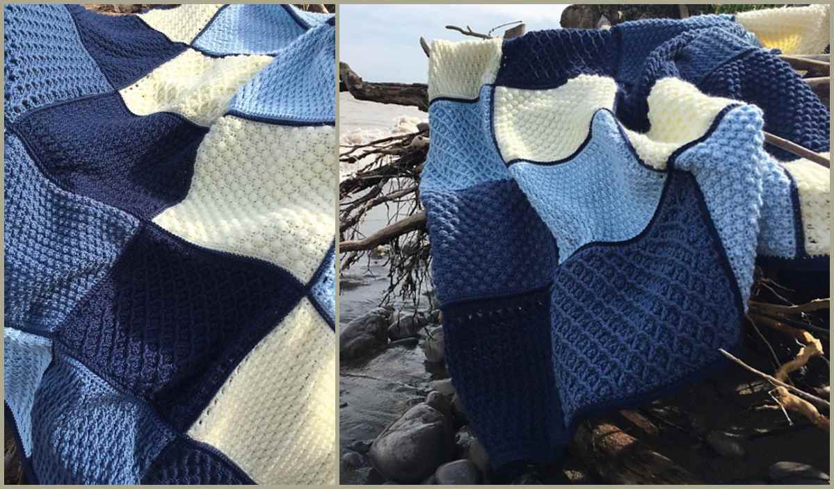 The Erie Water Throw, a blue and cream crochet blanket with textured squares, drapes elegantly over driftwood on the rocky beach.