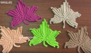 Five crocheted leaves in different colors, including pink, green, and beige, arranged on a wooden surface, reminiscent of the Butterfly Effect in nature.