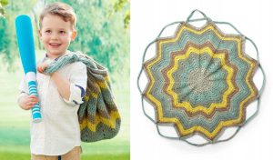 A child grips a blue baseball bat, their other hand clutching a crocheted handy bag. Beside them, a circular mat showcases an earthy starburst crochet pattern, adding charm to the scene.