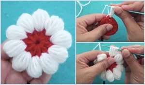 Close-up of hands crocheting a white and red puff stitch flower pattern with a hook on a blue surface.