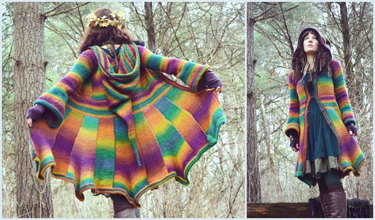 A person in a colorful, striped elf coat stands in a wooded area. The coat, resembling a crochet pattern with its hood and flared hem, complements the wreath on their head.