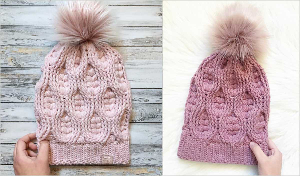 Pink knitted beanie with a pom-pom on top, reminiscent of an origami rose, displayed against wood and white backgrounds.