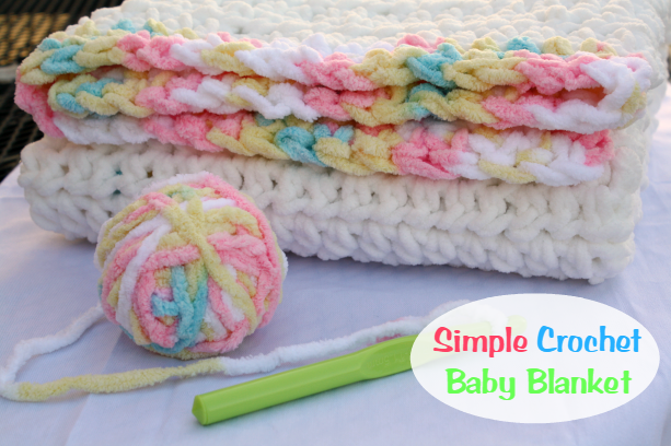 A folded crocheted baby blanket with pastel and white yarn, a matching yarn ball, and a green crochet hook on a white surface. Text reads 