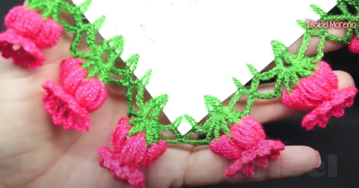 A hand holding a decorative crochet border showcases vibrant pink flower patterns with green leaves, highlighting a calming and artistic touch. Ideal for enthusiasts, discover the beauty of crochet flower edging free patterns that add elegance to your project.