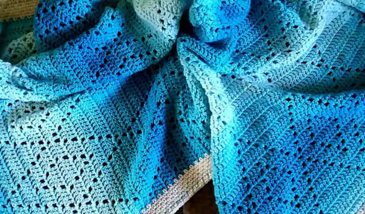 A crocheted blanket in shades of blue showcases an intricate crochet pattern displayed on a surface.