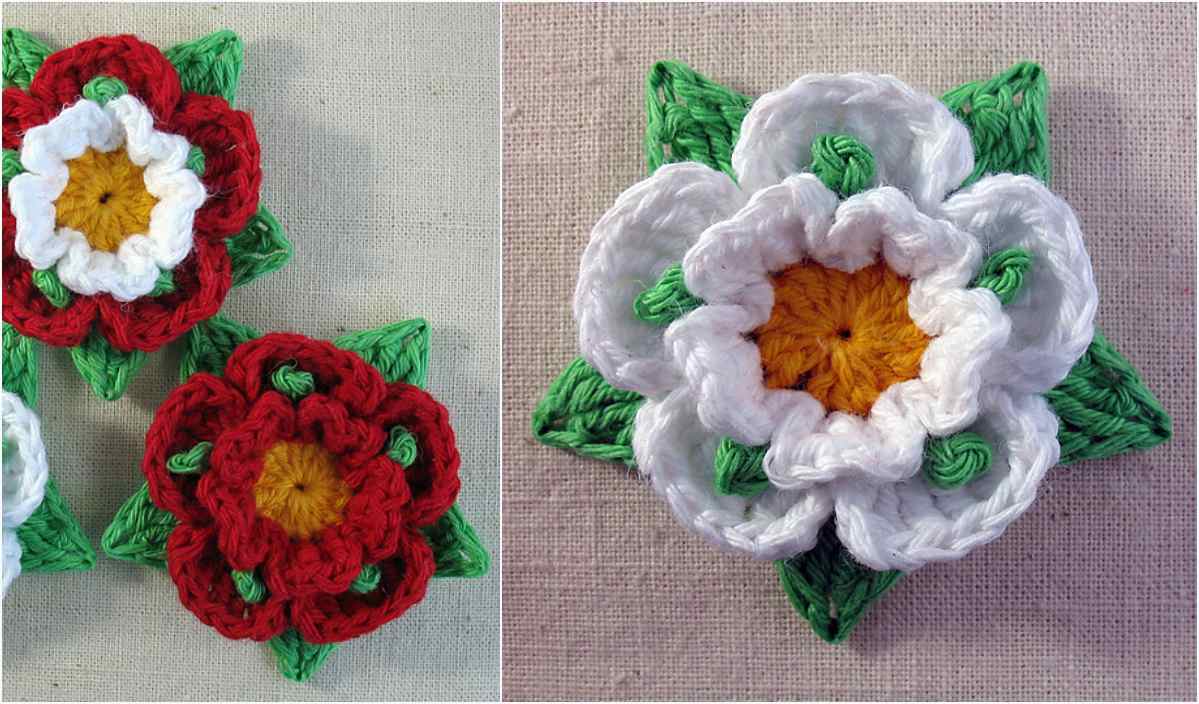 Crocheted flowers with red and white petals, yellow centers, and green leaves are elegantly displayed on a beige surface, showcasing a beautiful crochet pattern.