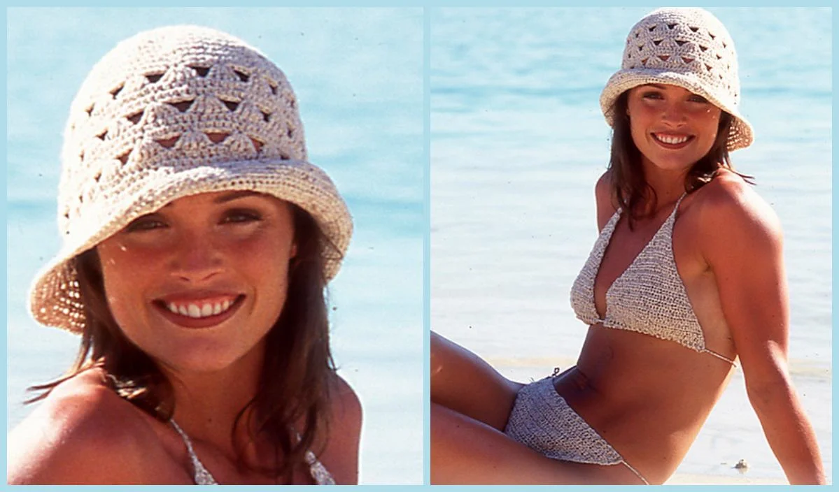 A woman in a woven hat and crochet bikini, perhaps inspired by a free crochet pattern, smiles at the camera while sitting on a beach with light blue water in the background.