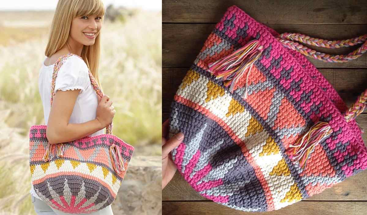 A smiling person holds a colorful crocheted bag with geometric patterns in shades of pink, gray, yellow, and white, featuring tassels and braided straps. Inspired by a free crochet pattern, it embodies vibrant creativity.