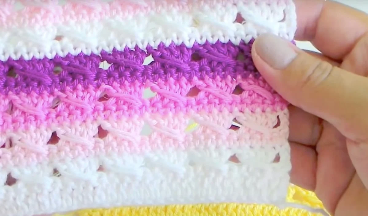 Hands skillfully holding a crochet sample featuring alternating stripes of white, pink, and purple yarn. Discover the beauty of each color with a free crochet pattern tutorial that guides you through every slip stitch with ease.