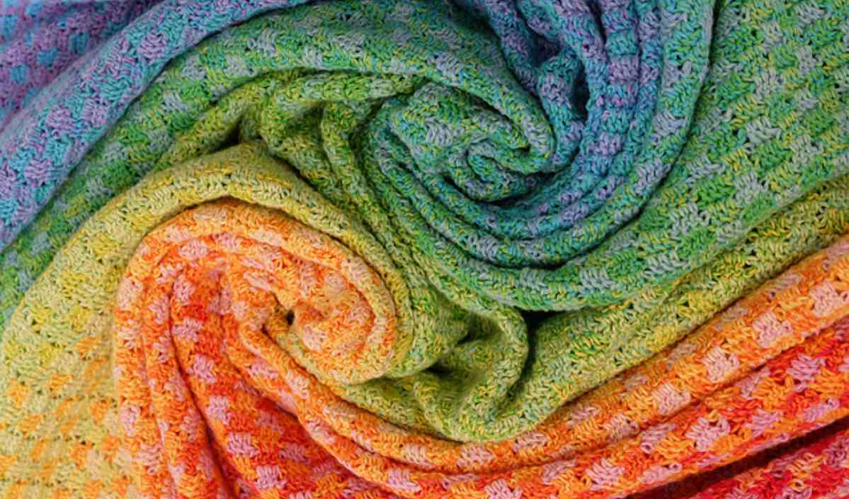 Close-up of a multicolored woven fabric featuring spiraled sections in shades of green, orange, blue, and purple, reminiscent of an intricate crochet pattern.