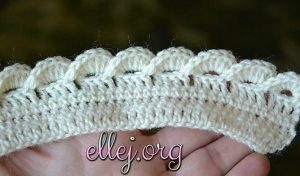 A close-up of a hand holding a crocheted piece with a scalloped edge pattern, reminiscent of a petal flower mandala.