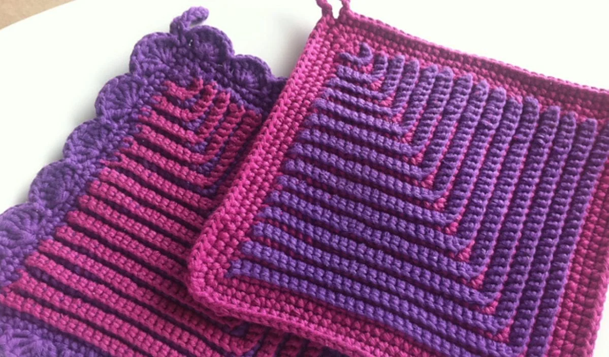 These German potholders feature a striking combination of purple and magenta, adorned with striped and scalloped edges. Perfectly displayed on a white surface, these pieces come with a free crochet pattern to inspire your next creation.