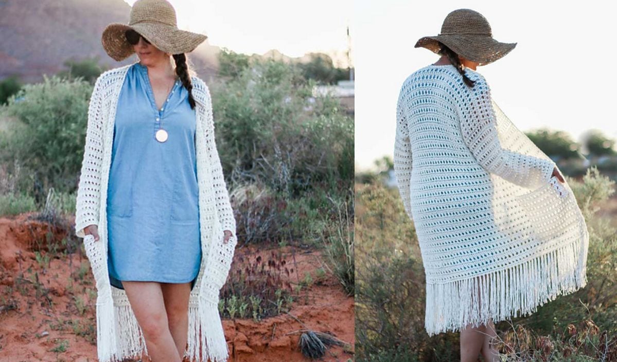 A woman in a blue dress, wide-brimmed hat, and Solstice Long Cardigan stands outdoors surrounded by desert plants.