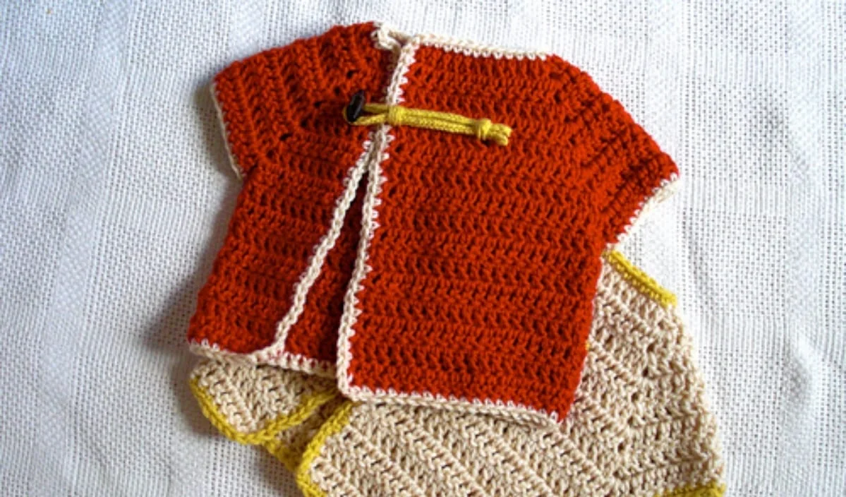 Discover this easy peasy crocheted baby sweater set, showcasing an orange jacket with a toggle button and matching beige pants. Perfect for those seeking free crochet patterns, this adorable baby cardigan makes a charming addition to your little one's wardrobe.